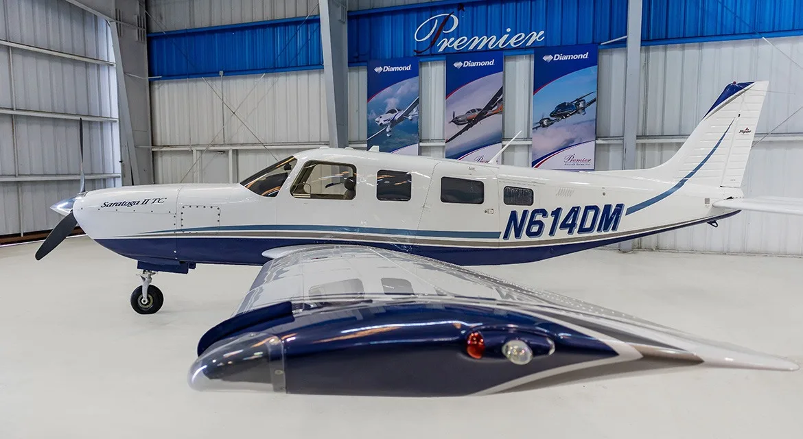 A side view of a white and blue Piper Saratoga II TC aircraft, registration N614DM, with its wing in the foreground.