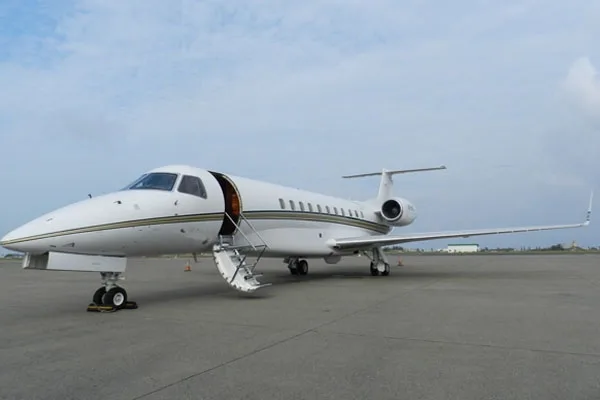 A white business jet with gold and black stripes is parked on an airfield with its main door open.