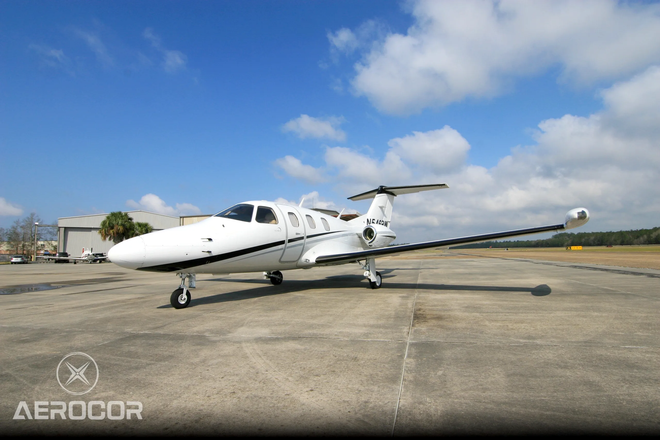 A white Eclipse 500 jet with black and grey stripes parked on an airfield under a blue sky.