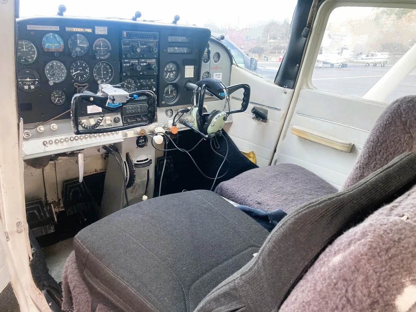 A view from the pilot's seat of a Cessna 182 cockpit, showing the instrument panel, controls, and front seats.