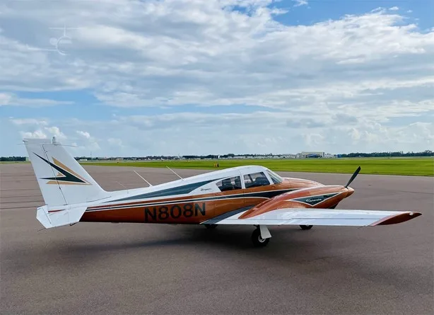 Side view of a copper and white Piper Comanche twin-engine aircraft with registration N808N on an airfield.