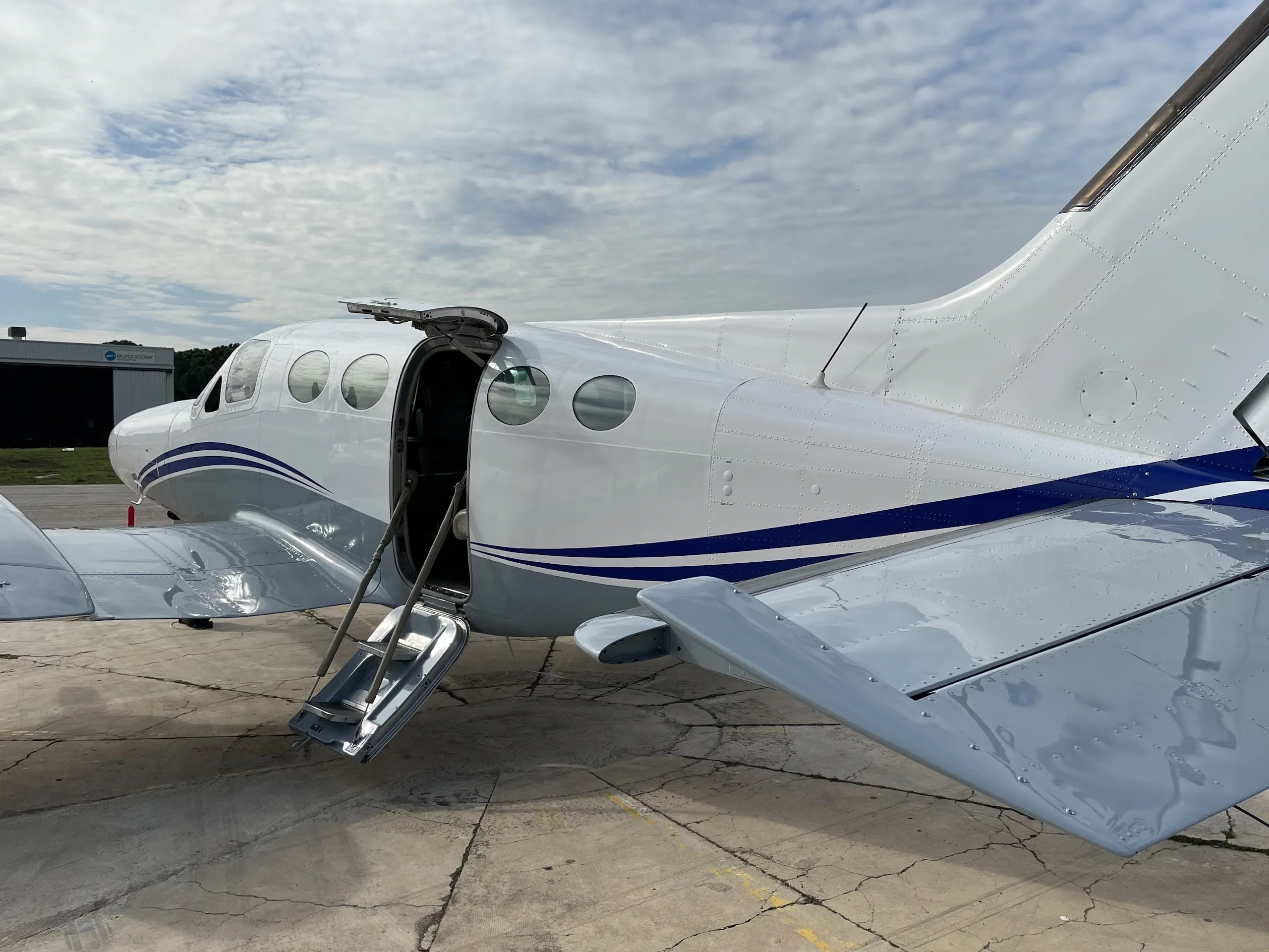 A close-up of the rear fuselage of a white and grey aircraft with blue stripes, showing the open passenger door with integrated stairs.