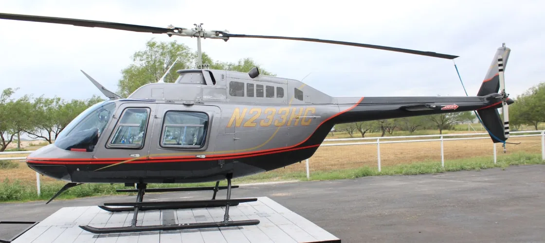 A grey and black Bell 206 JetRanger helicopter with registration N233HG is parked on a paved surface.