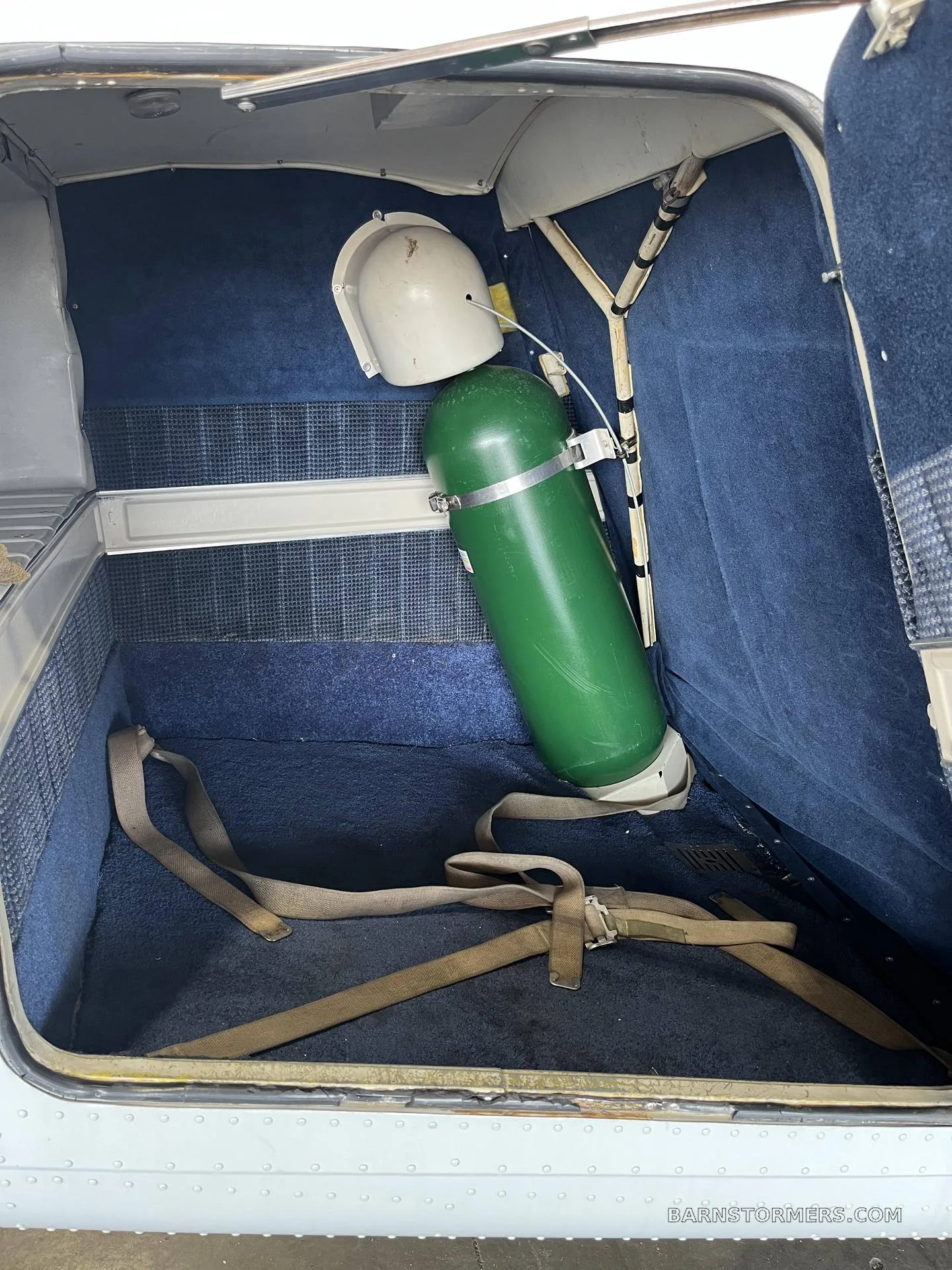 An aircraft's interior storage compartment with a green oxygen tank and securing straps.