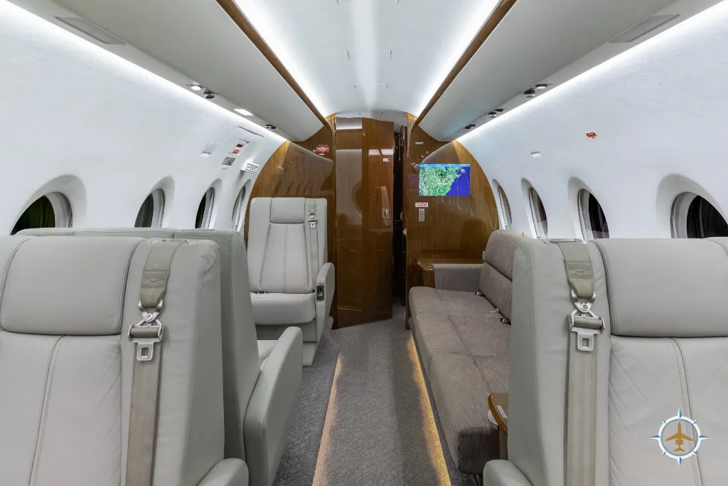 A view of the business jet cabin interior, featuring light grey seats and a long beige sofa.