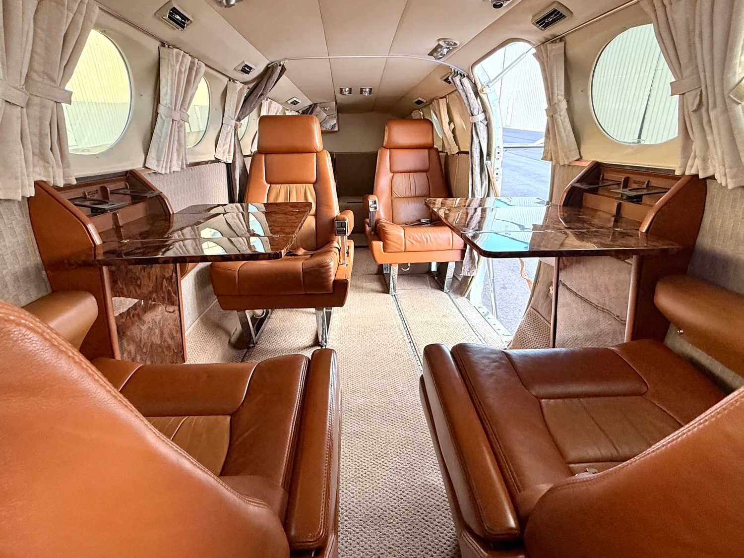 The aircraft's cabin interior with brown leather seats, fold-out tables, and wood paneling.