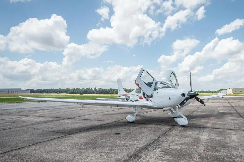A white Cirrus SR22 aircraft, registration N241LL, with its gull-wing doors open, parked on an airfield.