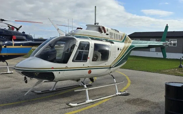 A white and green Bell 206 JetRanger helicopter is parked on an asphalt ramp under a cloudy sky.