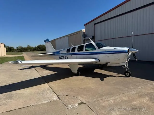 A white and blue Beechcraft Baron N1124A parked on an airfield with a hangar in the background.