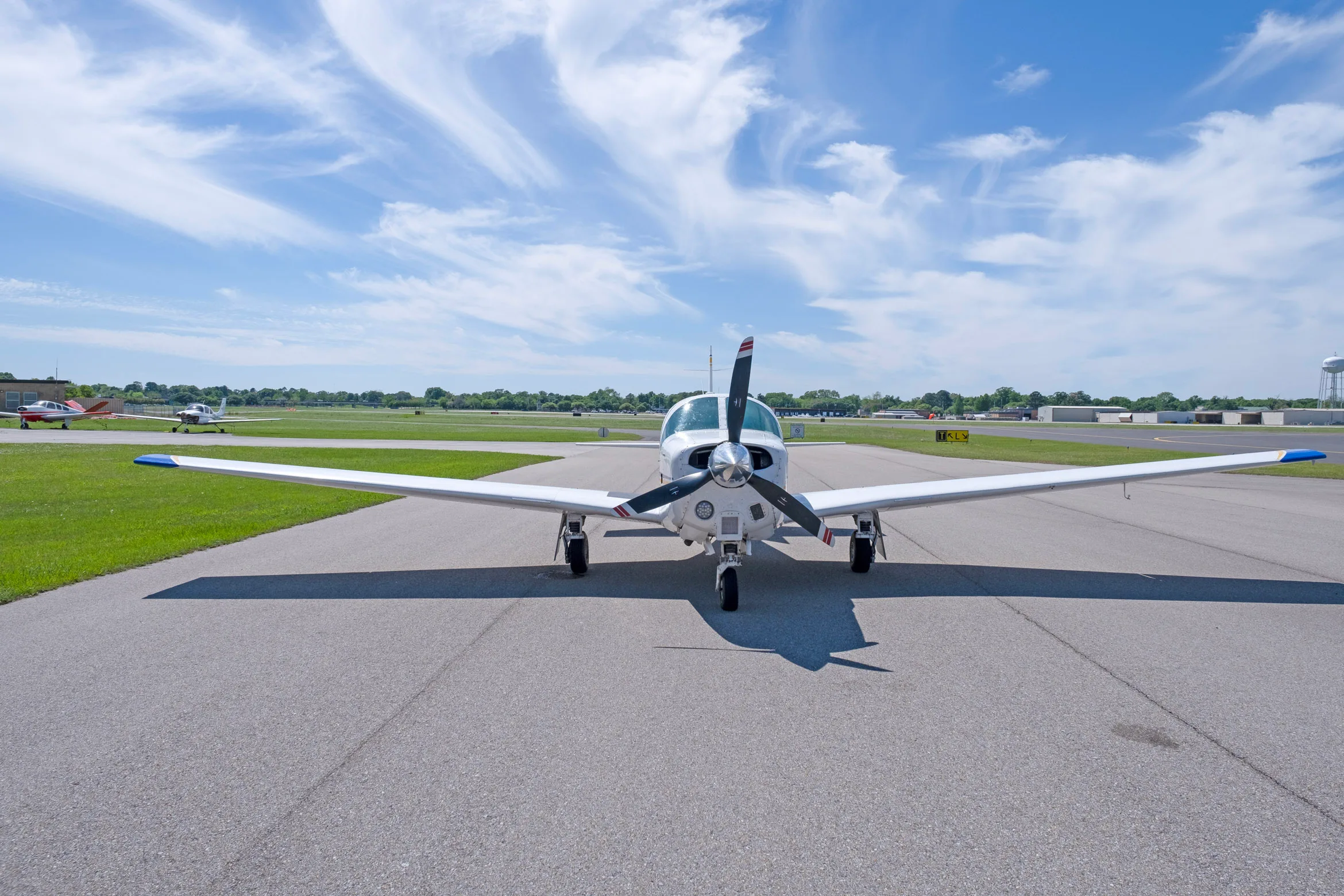 A front view of a white single-engine propeller aircraft with blue and yellow stripes, registration N1957Y, parked on an asphalt runway.