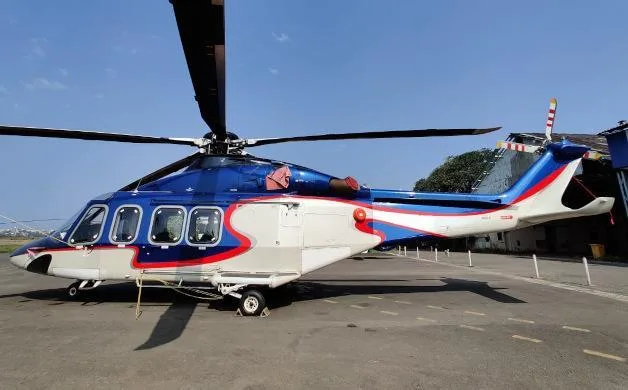 A blue, white, and red AgustaWestland AW139 helicopter is parked on an asphalt pad under a clear sky.