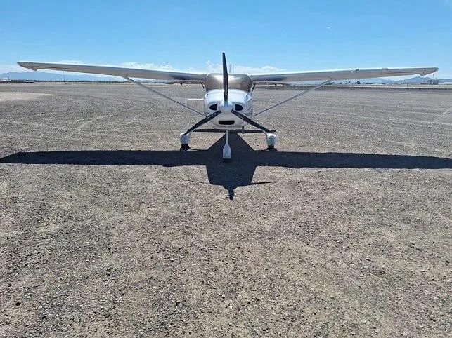 A head-on view of a white Sirius LightSport aircraft with a propeller, parked on an airfield.