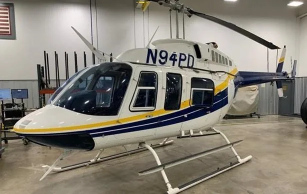 A white and blue helicopter with yellow stripes, registration N94PD, parked in a hangar.