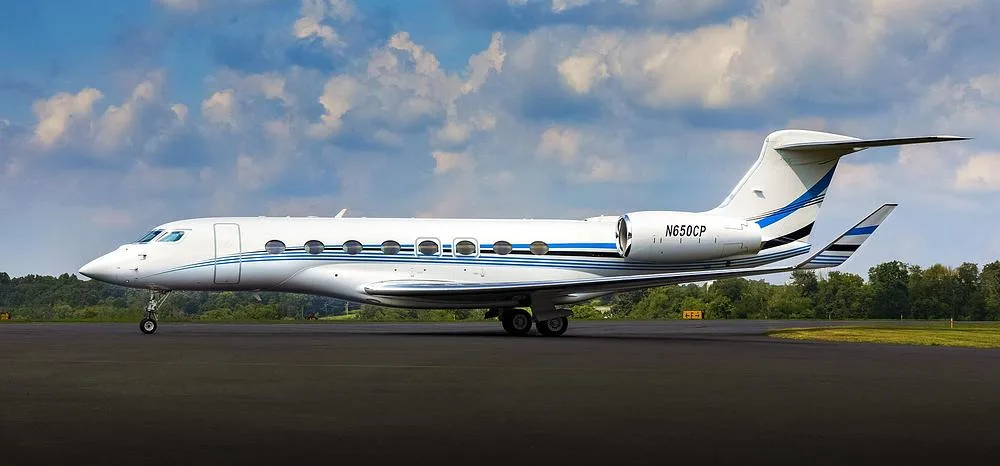 A white Gulfstream G650 business jet with blue and black stripes and registration N650CP parked on an tarmac.