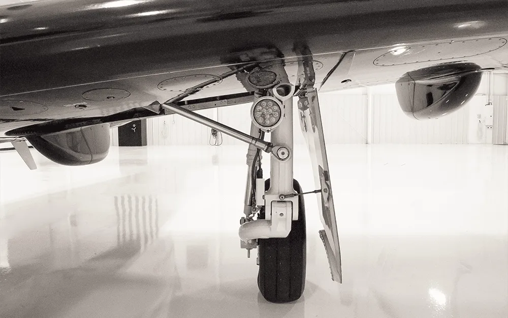 Black and white close-up of the main landing gear and undercarriage of a Pilatus PC-12 aircraft.
