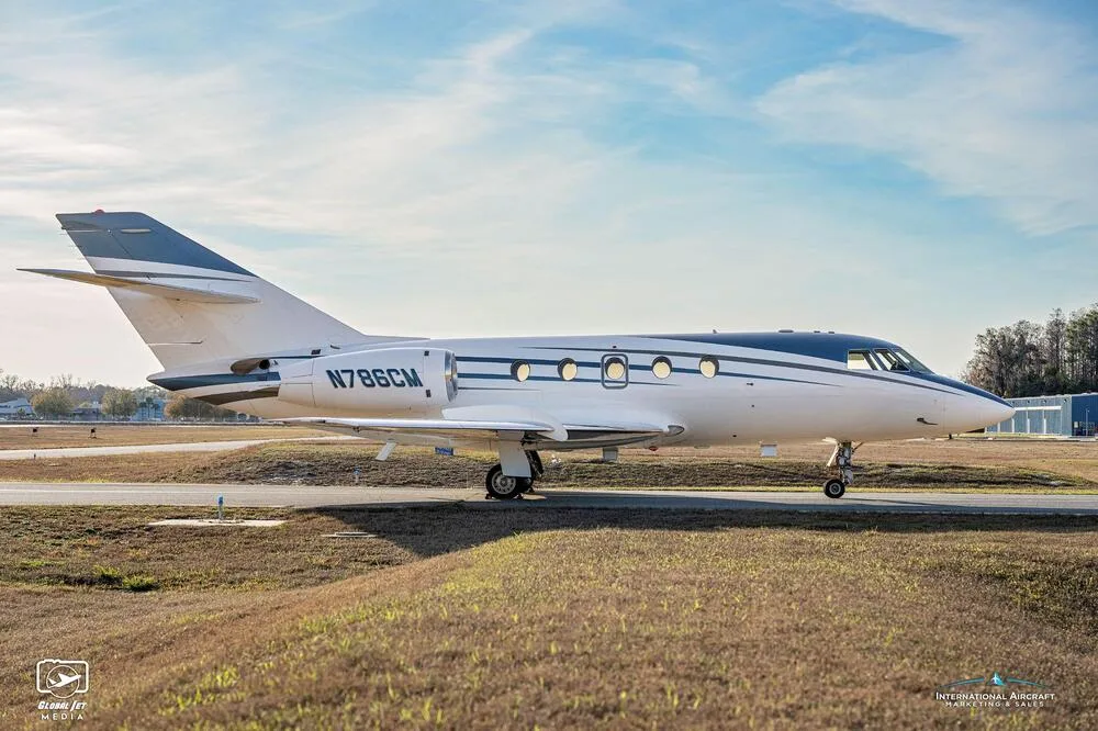 A side view of the white and blue business jet N786CM on a tarmac under a partly cloudy sky.