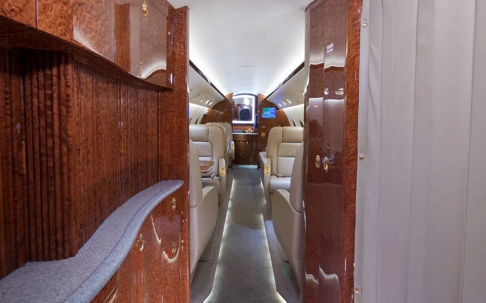 A view down the aisle of a luxurious aircraft cabin with wood paneling and tan leather seats.