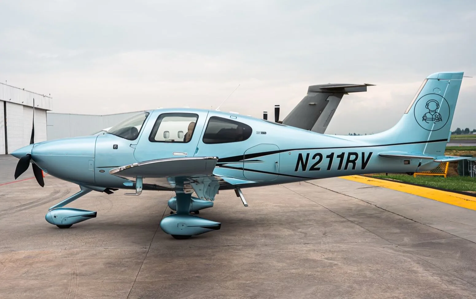 A light blue Cirrus SR22T aircraft with registration N211RV parked on an airfield, showing the right side.