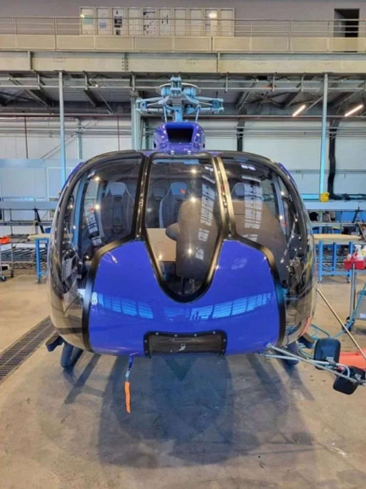 A blue Airbus H135 helicopter with skids, seen from the front in a hangar.