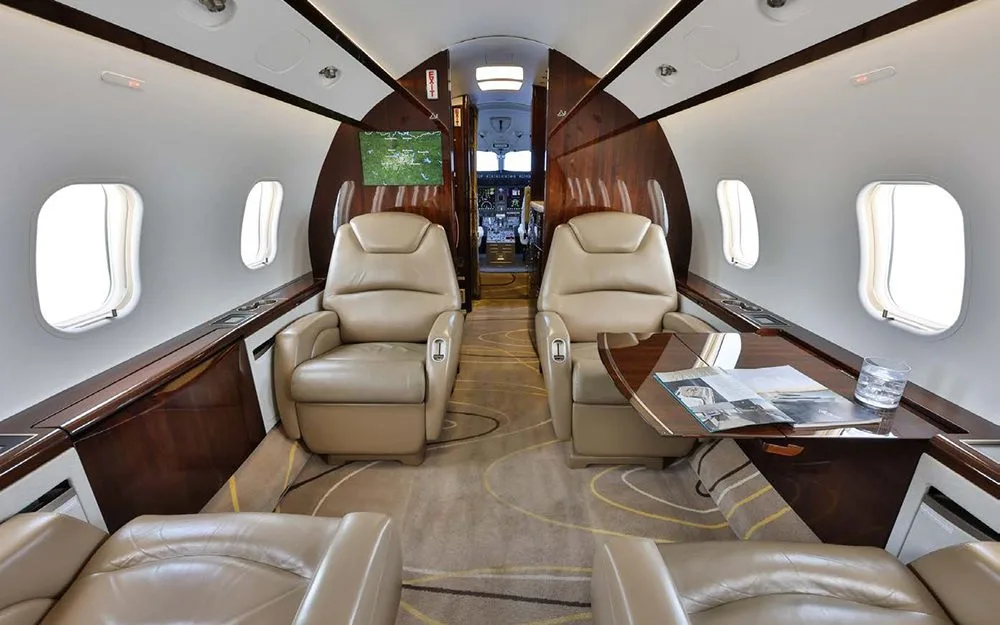 The luxurious interior cabin features tan leather seats, wood paneling, and a view towards the cockpit.