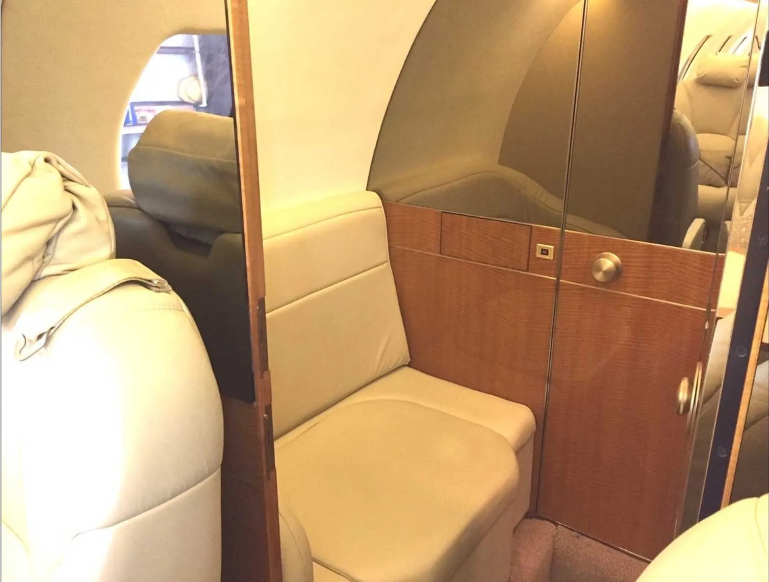A section of the aircraft interior with a beige bench seat, wood paneling, and a mirrored surface.