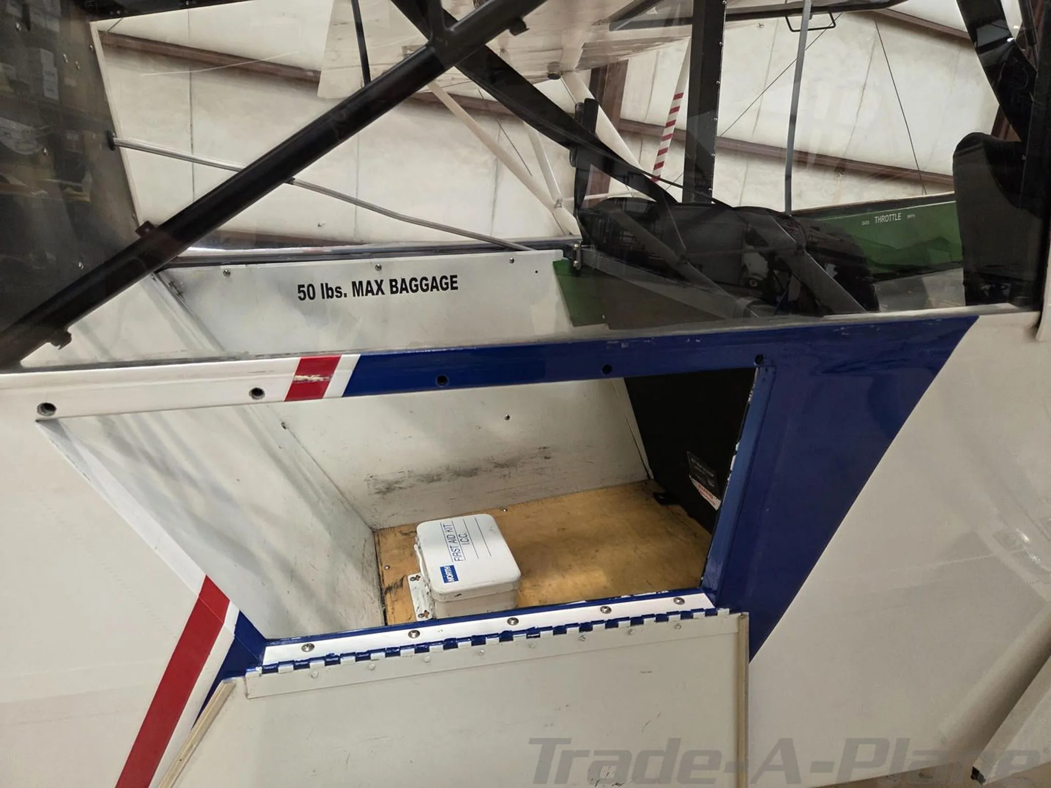 View of the open baggage compartment of the Piper Super Cub, showing a white container and a '50 lbs. MAX BAGGAGE' label.