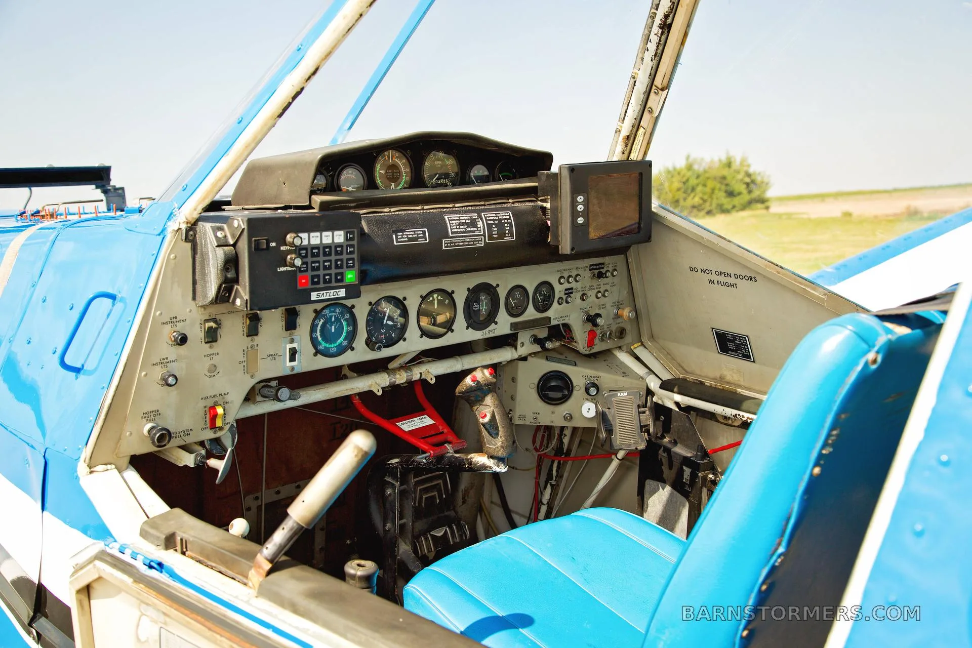 The cockpit of a blue and white agricultural aircraft, showing the instrument panel, controls, and a blue seat.