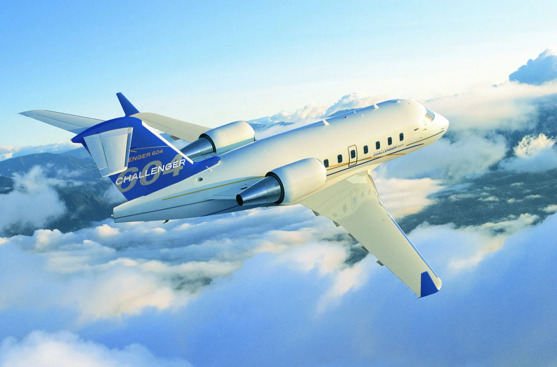 A white and blue Bombardier Challenger 604 business jet flies above clouds with mountains in the background.