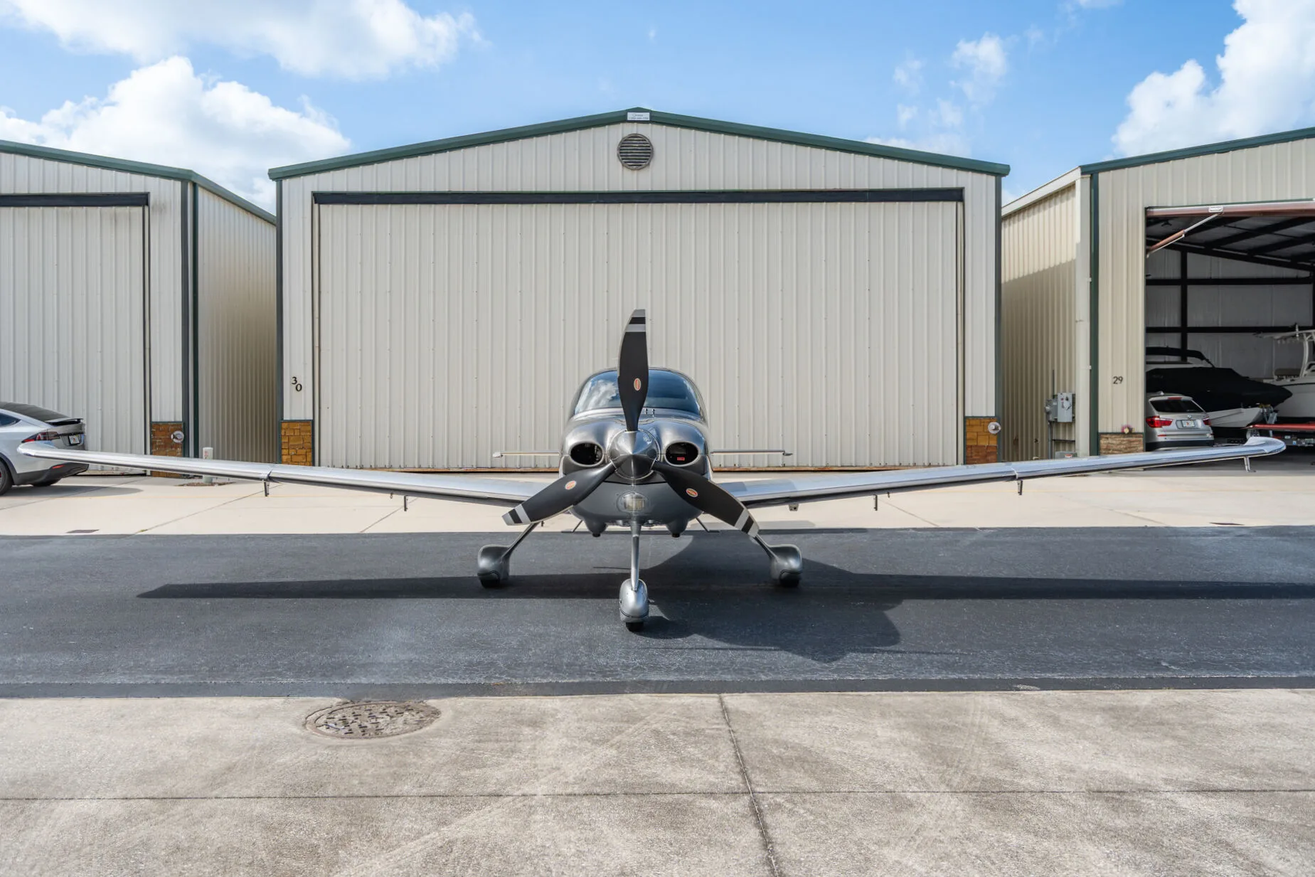 Front view of a silver Cirrus SR22T aircraft (N3404) parked on an airport tarmac in front of hangars.