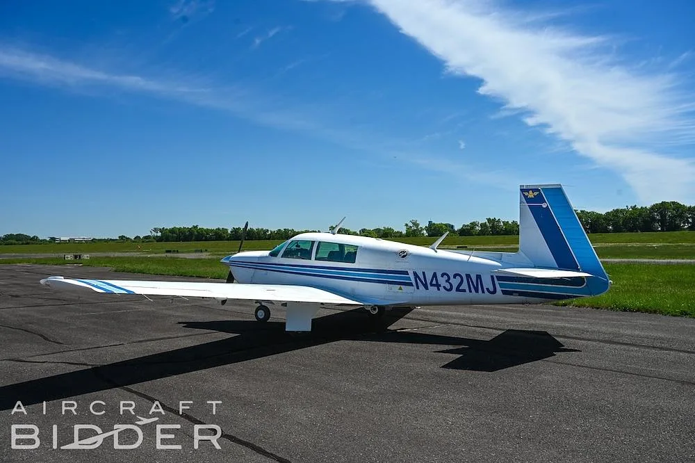 A white single-engine propeller aircraft N432MJ with blue stripes is parked on an asphalt runway, viewed from the side.