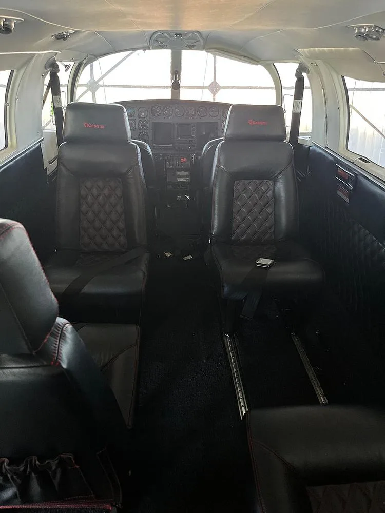 The aircraft's interior, showing two black leather front seats with red stitching and the instrument panel beyond.