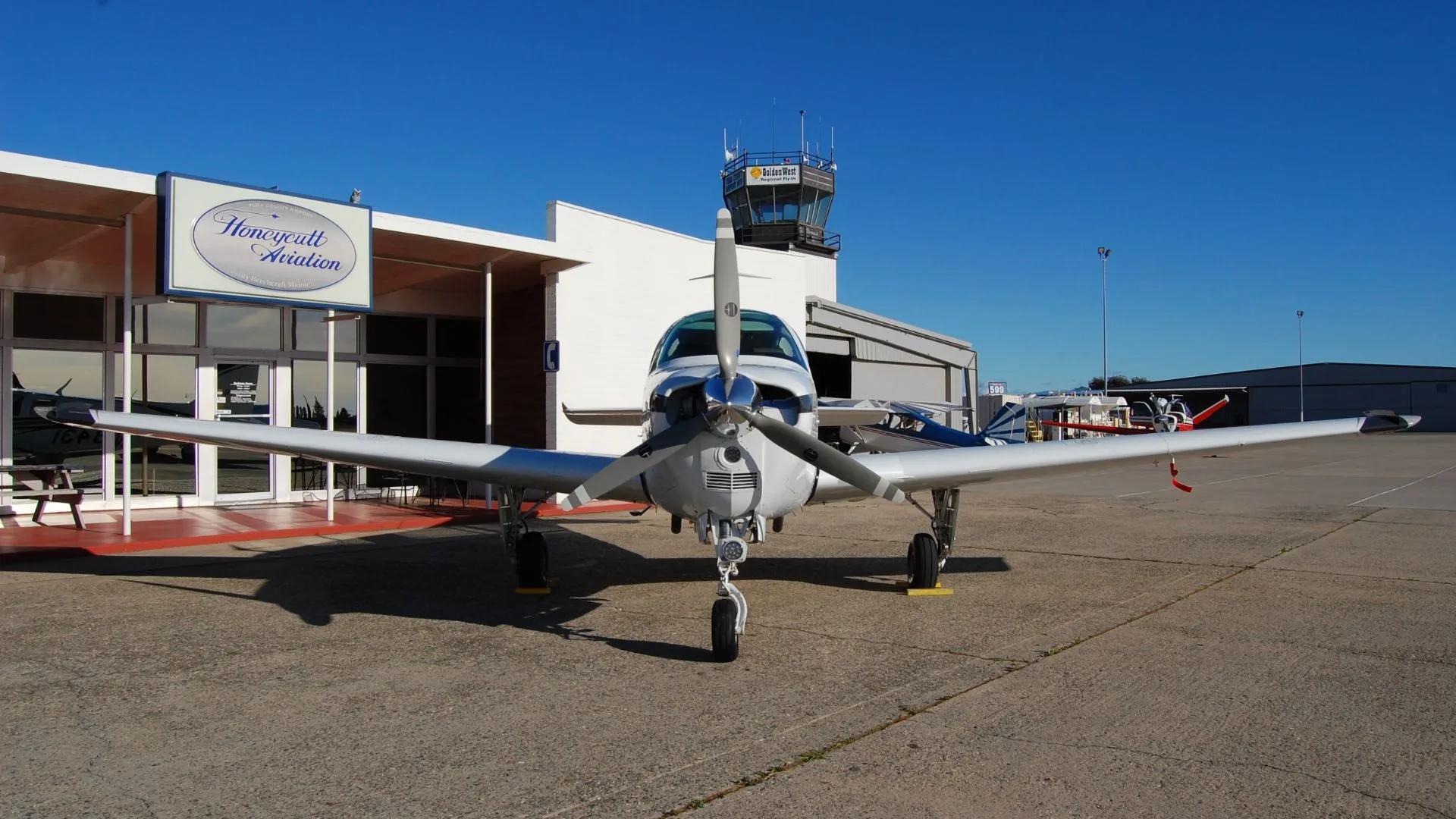 Front view of a Beechcraft Bonanza parked on the tarmac in front of a building.
