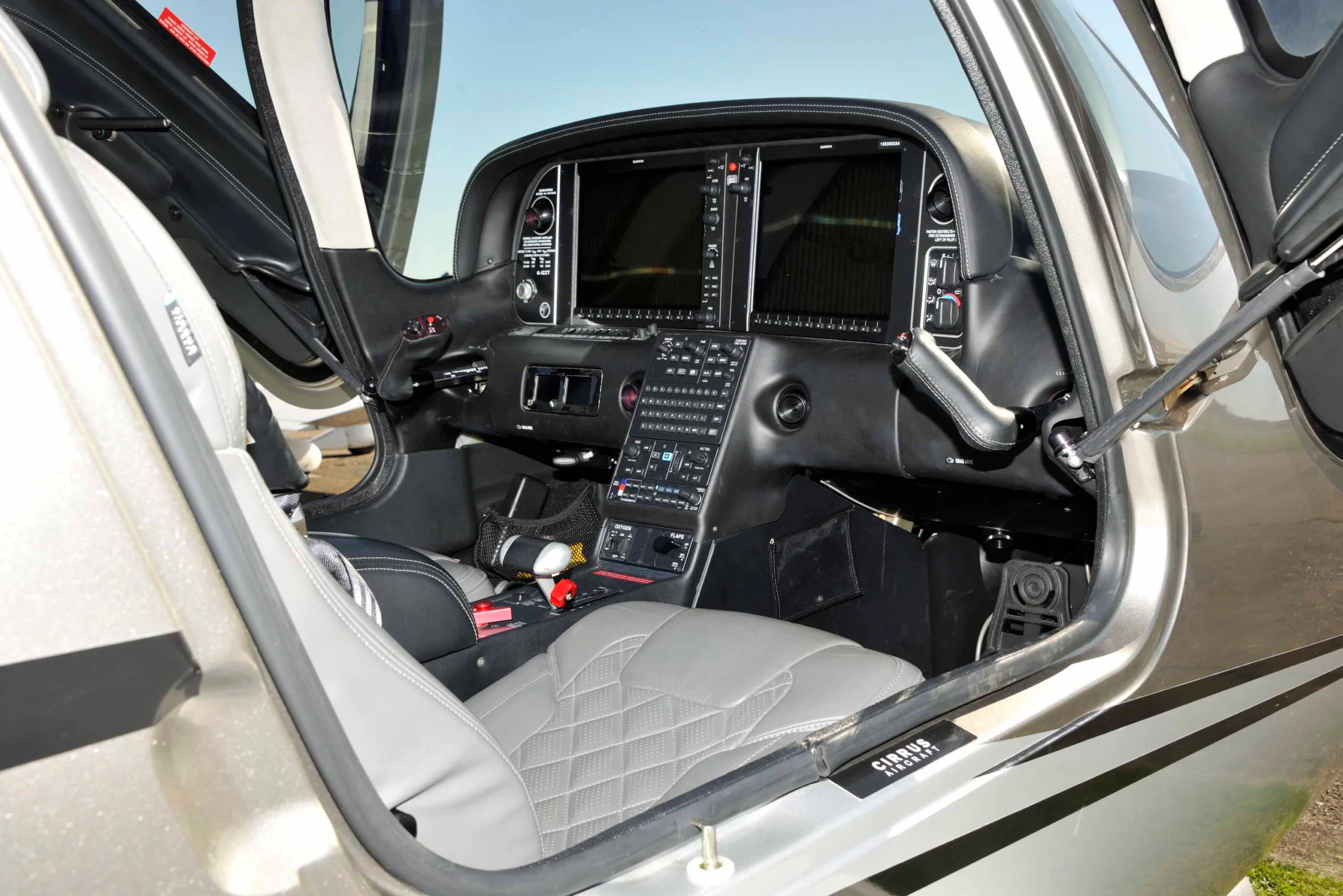The cockpit of a Cirrus SR22T showing the instrument panel with screens off and grey quilted seats.