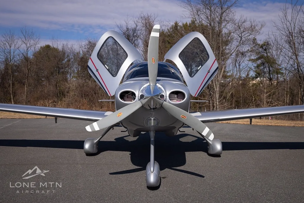 Front view of a silver Cirrus SR20 aircraft with registration N975TK, showing its propeller and open doors.