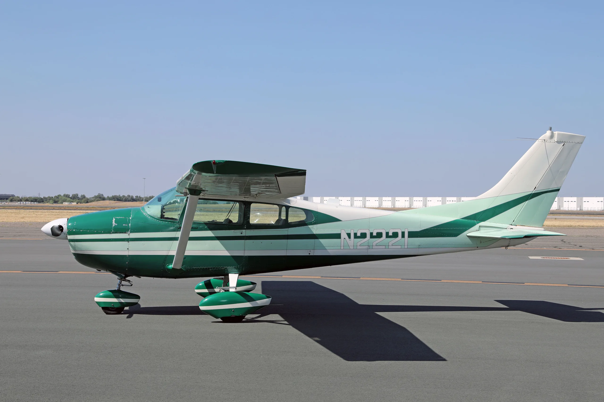 A side view of a green and white Cessna 182 Skylane N2221 with its wing flaps extended on an airfield.