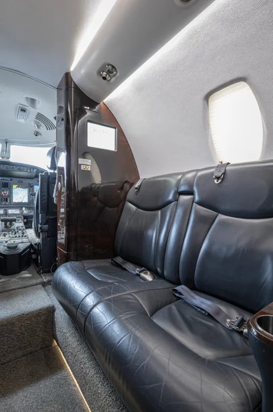 A black leather bench seat in the aircraft cabin, with the cockpit visible through an open doorway.