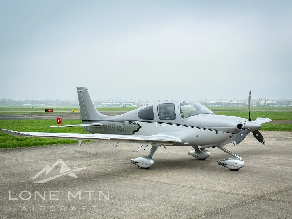 A silver Cirrus SR22 aircraft, registration N6918C, parked on an airfield with runway markings visible.