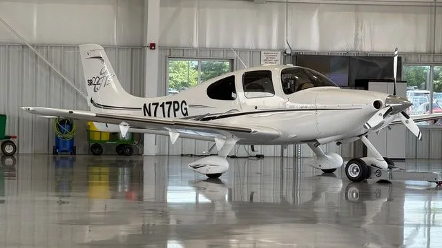 White Cirrus SR22T aircraft N717PG with black and grey stripes parked inside a hangar.
