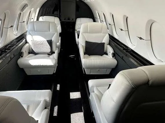 The luxurious interior of a private jet cabin, featuring white leather seats with black pillows and a dark aisle.