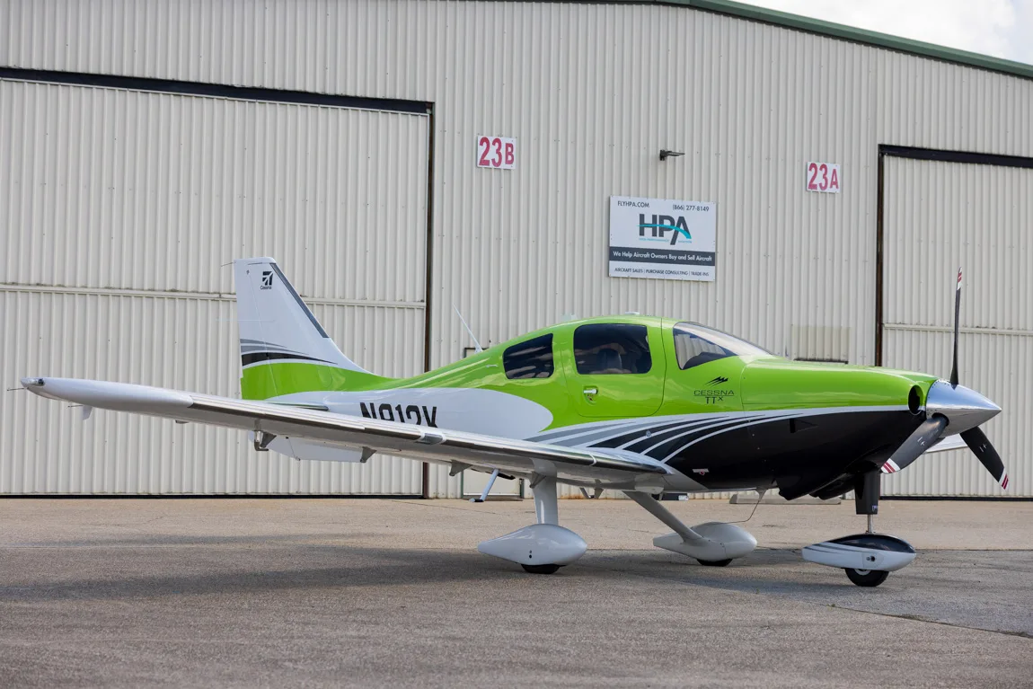 A lime green, white, and black Cessna TTX aircraft with registration N101V parked in front of a hangar.