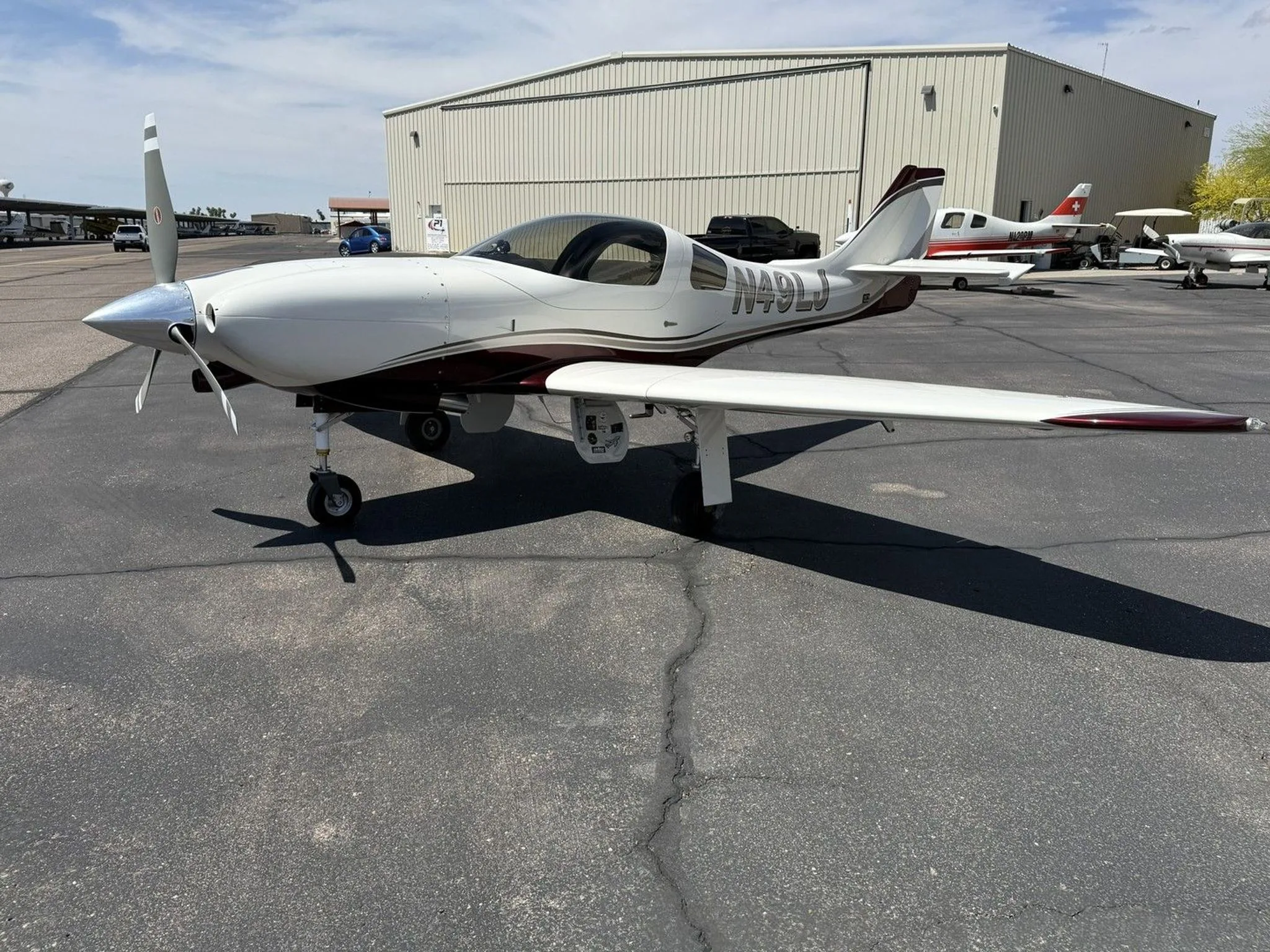 A white and maroon single-engine aircraft (N49LJ) parked on an asphalt apron with other aircraft in the background.