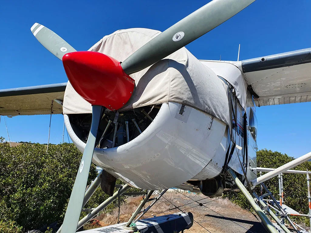 A close-up view of the front of a white seaplane, showing the red propeller spinner, grey propeller blades, and engine cowl cover.