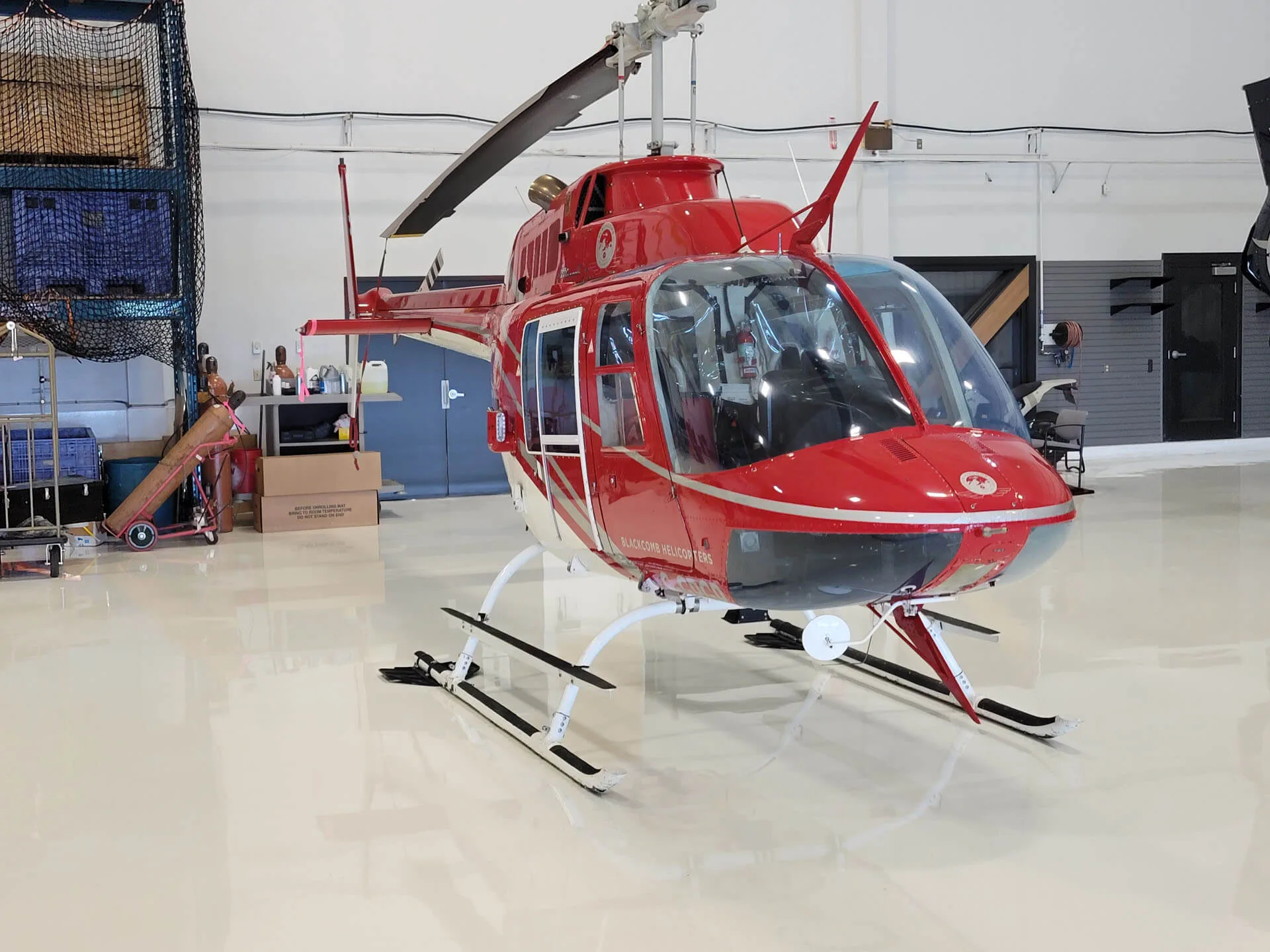 A red and white helicopter with skis on its landing gear is parked inside a brightly lit hangar.