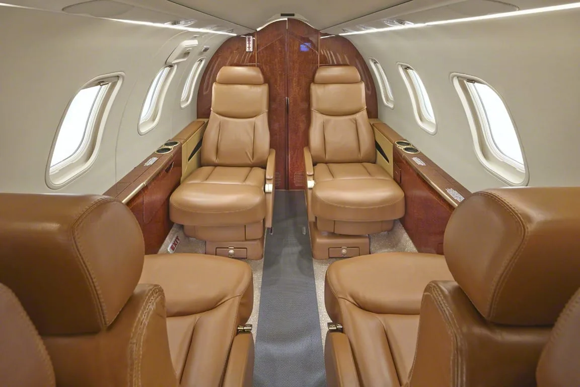 A view of the private jet cabin showing tan leather seats and wood paneling.