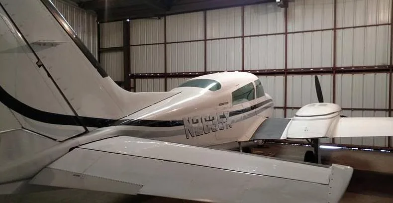 Rear-left view of a white twin-engine aircraft, N2635X, with black and gray stripes, inside a hangar.