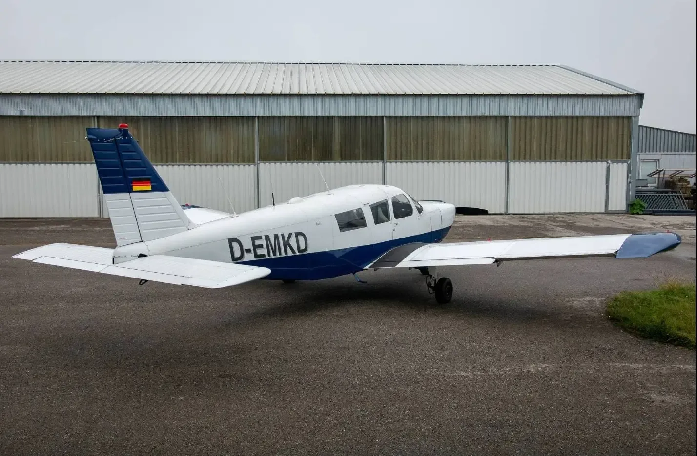 A white and blue single-engine propeller aircraft (D-EMKD) viewed from the rear-right, parked on an asphalt apron.