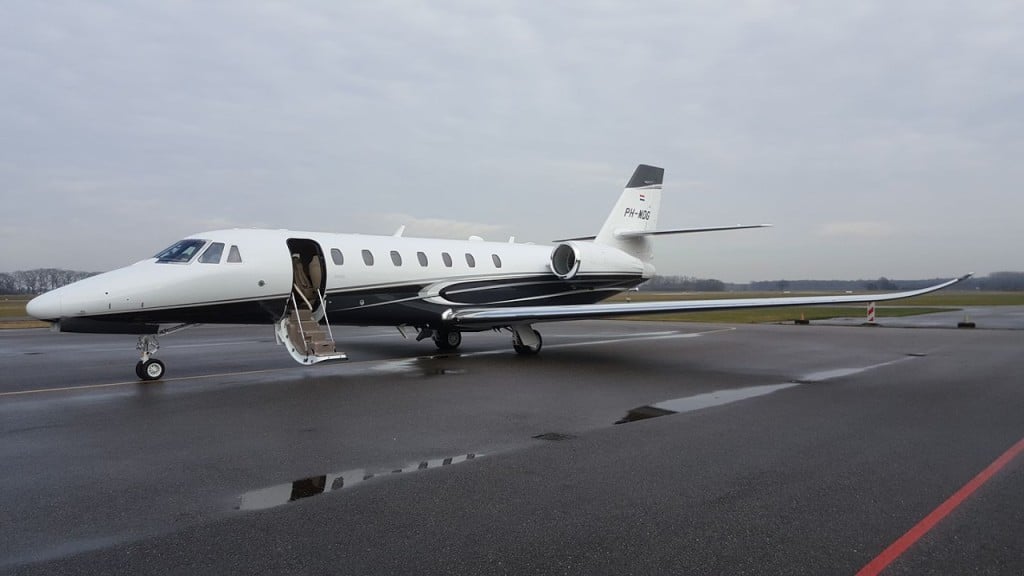 A white and black aircraft with the door open on a wet tarmac.