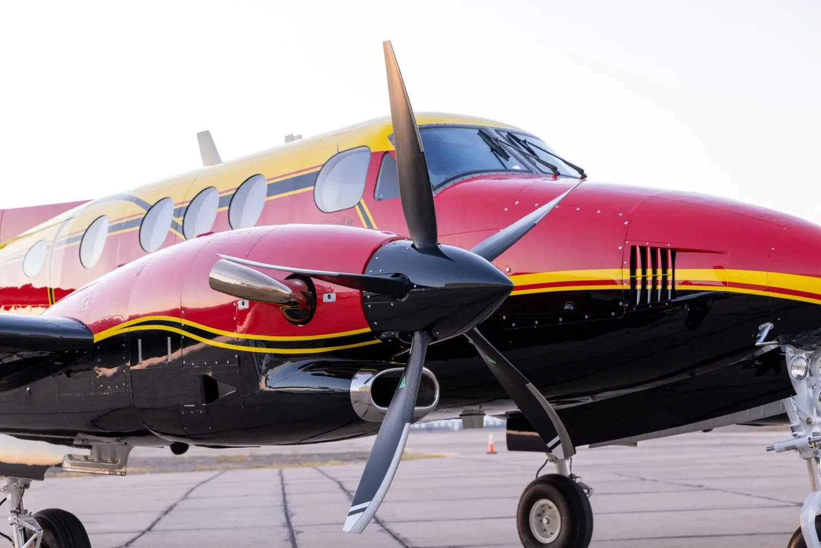 A close-up view of the left engine and propeller of a red, yellow, and black King Air C90B.