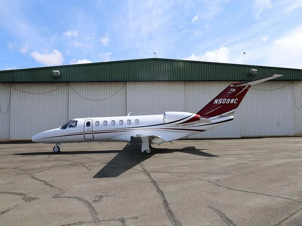 A white private jet with red and black accents, tail number N509WC, parked on an tarmac in front of a hangar.