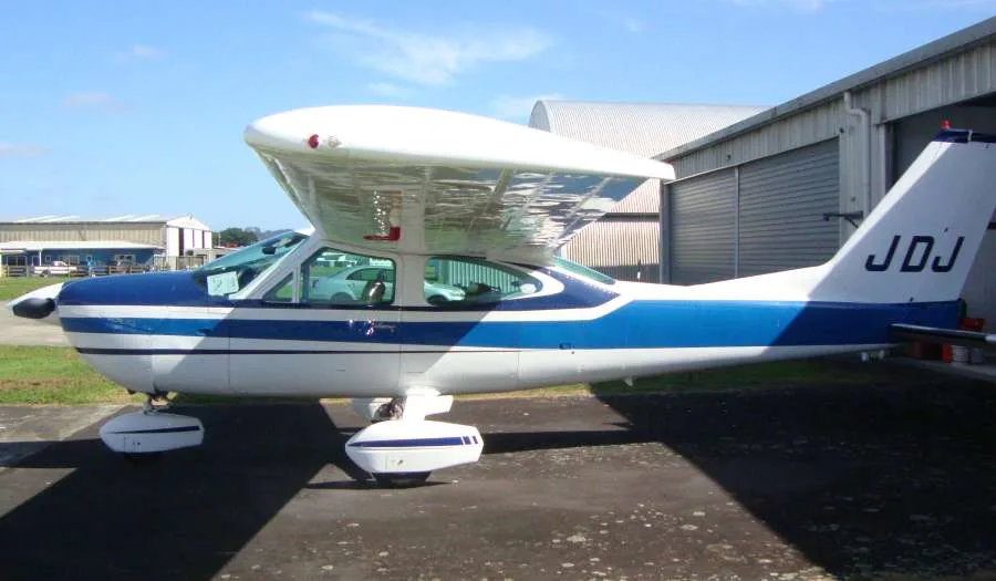 A white and blue single-engine aircraft with tail number JDJ parked outside a hangar.
